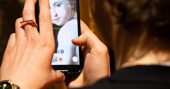 Fotografia: osoba z tyłu robi telefonem zdjęcie portretu; na ekranie zbliżona twarz