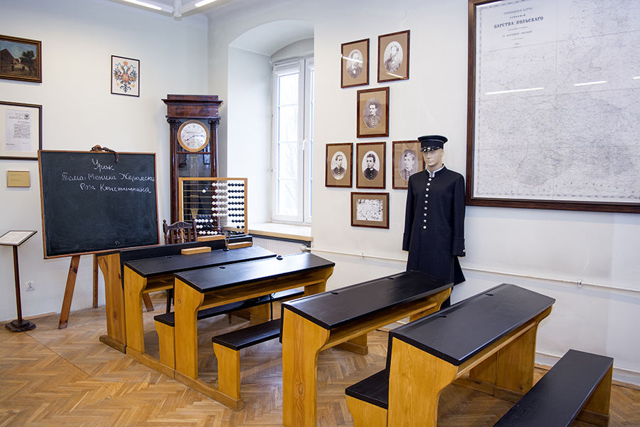 Dawna sala lekcyjna w Muzeum Lat Szkolnych Stefana Żeromskiego, na pierwszym planie ławki, dalej dawny mundurek szkolny