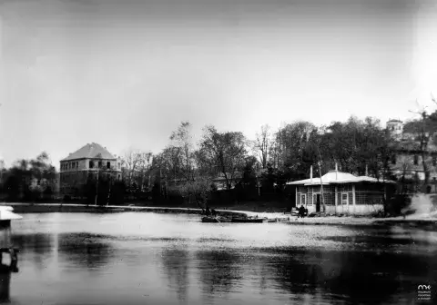 Czarno-biała fotografia nabrzeża z pawilonem, willami i spokojną taflą wody