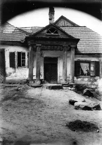 Czarno-biała fotografia zniszczonego domu z popękanym gankiem i gruzem na podwórzu