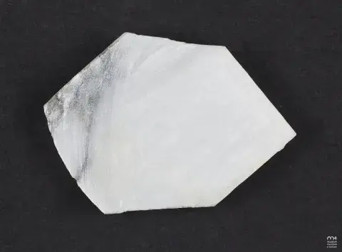 Fotografia nieregularnej, białej próbki minerału z połyskiem na czarnym tle
