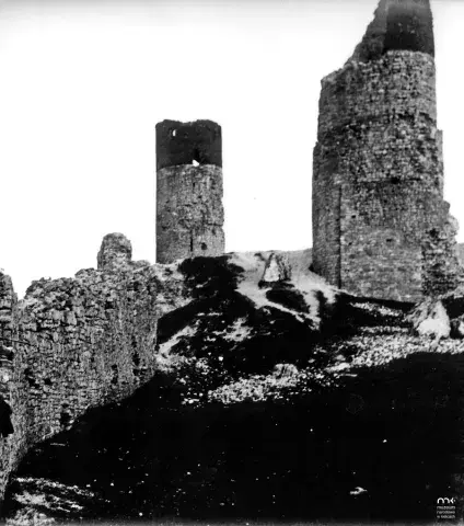 Czarno-biała fotografia ruin zamku z okrągłymi wieżami na skalistym wzgórzu