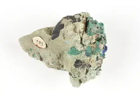 Fotografia minerału — zielono‑niebieskie kryształy na skale z małą papierową etykietą