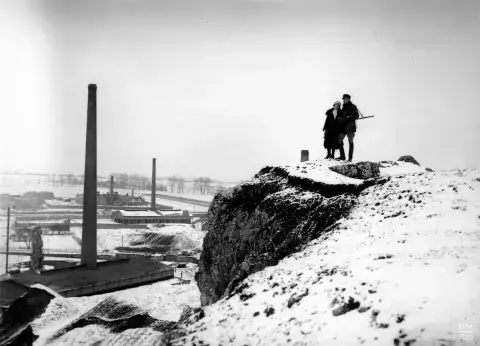 Fotografia: dwie osoby na śnieżnym urwisku nad zakładami przemysłowymi