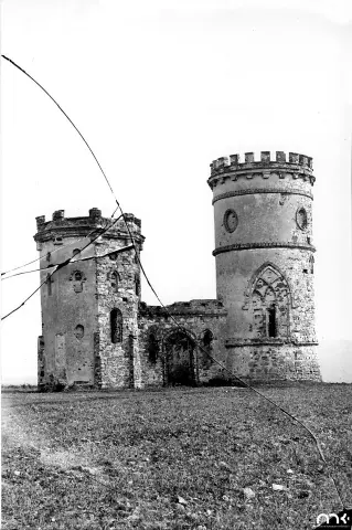 Czarno-biała fotografia ruin z kwadratową i okrągłą wieżą na polu