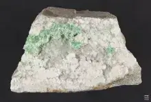 Fotografia kawałka skały z białymi kryształami i zielonymi minerałami w zagłębieniu