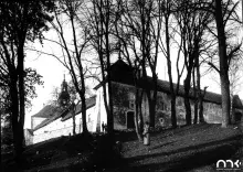Czarno-biała fotografia: budynek na wzgórzu, nagie drzewa, dwie postacie