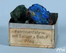 Fotografia: drewniane pudełko z niemiecką etykietą i dwoma niebiesko‑zielonymi minerałami