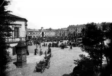 Czarno-białe zdjęcie historycznego rynku z ludźmi, ławkami i kamienicami