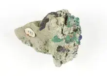 Fotografia minerału — zielono‑niebieskie kryształy na skale z małą papierową etykietą