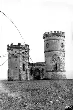 Czarno-biała fotografia ruin z kwadratową i okrągłą wieżą na polu